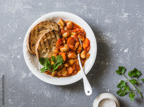 Stew beans in tomato sauce and grilled bread. Beans bruschetta. Delicious vegetarian appetizer on grey background, top view photo