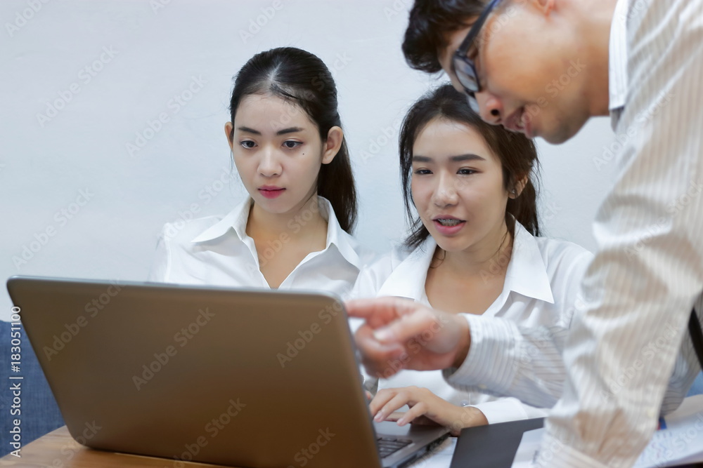 Young Asian business people working together on a laptop computer at office. Teamwork brainstroming concept. Selective focus and shallow depth of field. Young Asian business people working together on a laptop computer at office. Teamwork brainstroming concept. Selective focus and shallow depth of field.