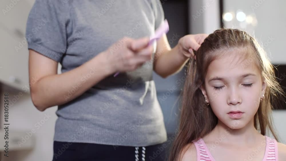 An attractive woman does her hairstyle for her little daughter. A woman is weaving a pigtail for her daughter.