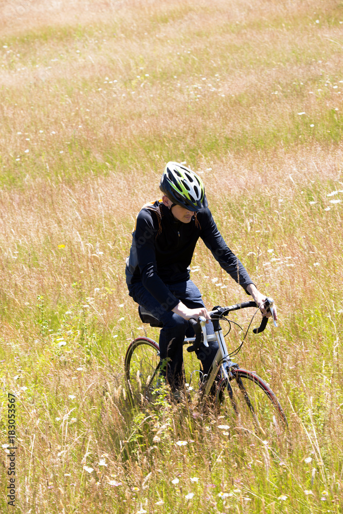 Cyclist in helmet rides through wild meadow with uncut grass Cyclist in helmet rides through wild meadow with uncut grass