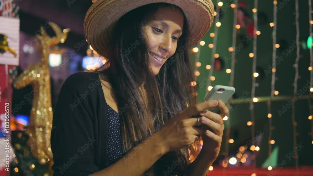 Young Mixed Race Hipster Girl Texting Greetings Messages on Smart Mobile Phone with Christmas Tree on Background. 4K. Young Mixed Race Hipster Girl Texting Greetings Messages on Smart Mobile Phone with Christmas Tree on Background. 4K.