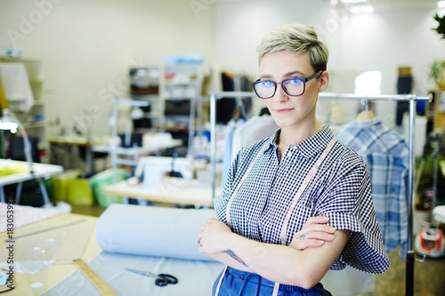 Modern seamstress in casualwear looking at camera by her workplace in tailoring-shop