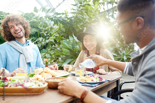 Happy friends gathered by breakfast or dinner in orangery or in the garden