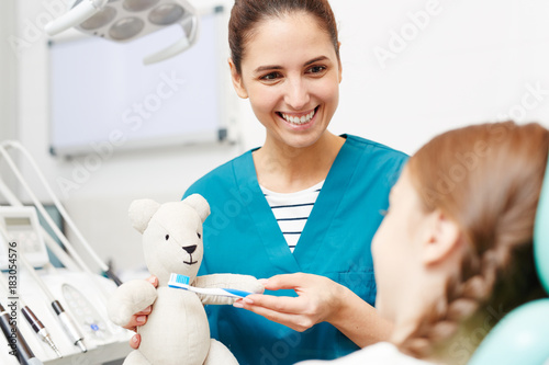 Smiling doctor showing little patient how it is important to brush teeth regularly and properly