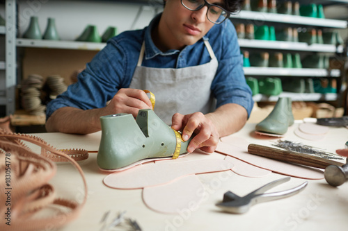 Bild auf Leinwand Contemporary cobbler measuring boot workpiece on table in his workshop