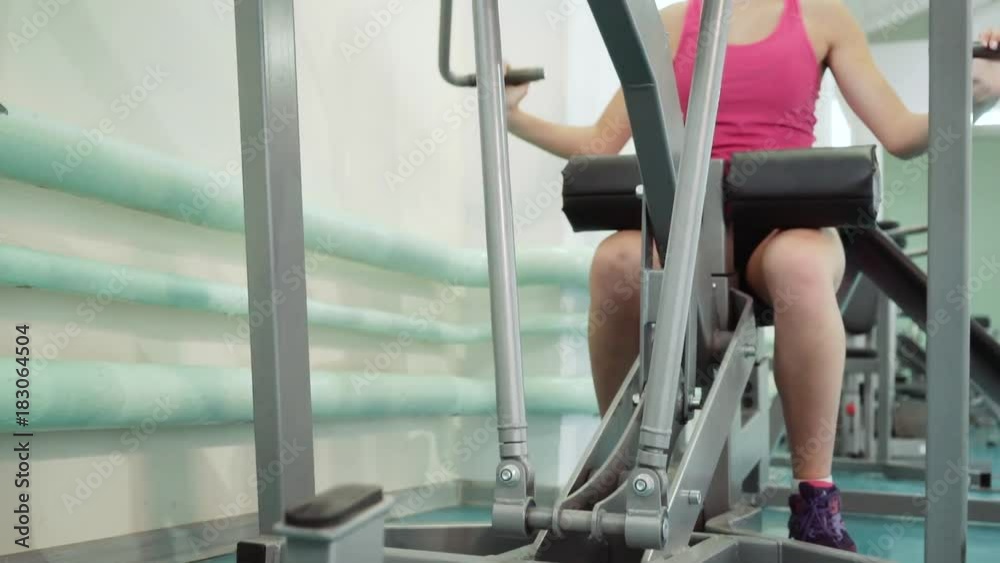 Thrust of the upper block. The girl is doing exercises on the simulator in the gym.