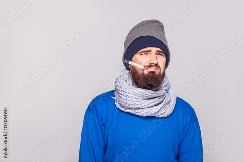 Young adult bearded man have temperature, holding thermometer in mouth.