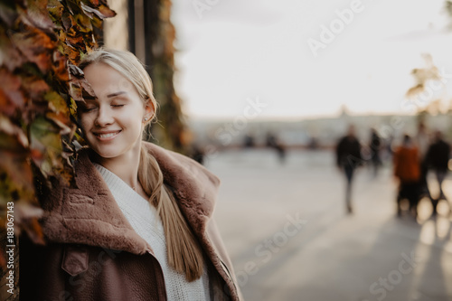 Outdoors fashion blonde young woman posing on the magical autumn leaves on background near building on the street