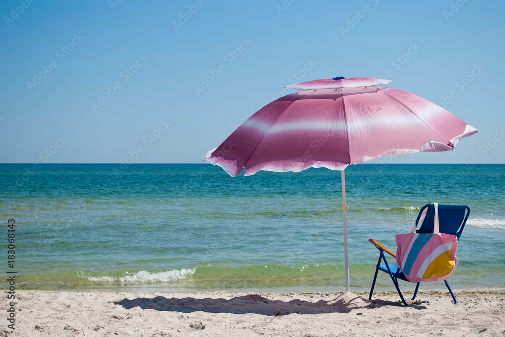 Blue beach chair and pink bag and pink big open umbrella for shade on the shore of the blue sea Island of sand in the water blue sky sea wave beautiful landscape summer vacation beach sand weekend