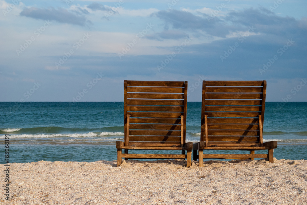 two wooden brown chaise longue on the beach on the blue sea shore water blue sky sea wave beautiful landscape summer vacation beach sand weekend rest