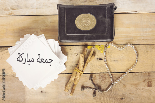 Canvas Print Jumah Mubarakah (=Friday Mubarak) in arabic and object muslim on wood table