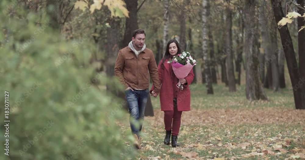 Loving couple walking in autumn forest park 4k video. Young man and woman with flower bouquet romantic date. Love story romance concept Loving couple walking in autumn forest park 4k video. Young man and woman with flower bouquet romantic date. Love story romance concept