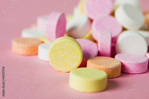 Close up of pile of chewable antacid acid indigestion relief tablets with fruit flavour in pastel colors, such as pink, yellow, orange and white on light pastel pink background