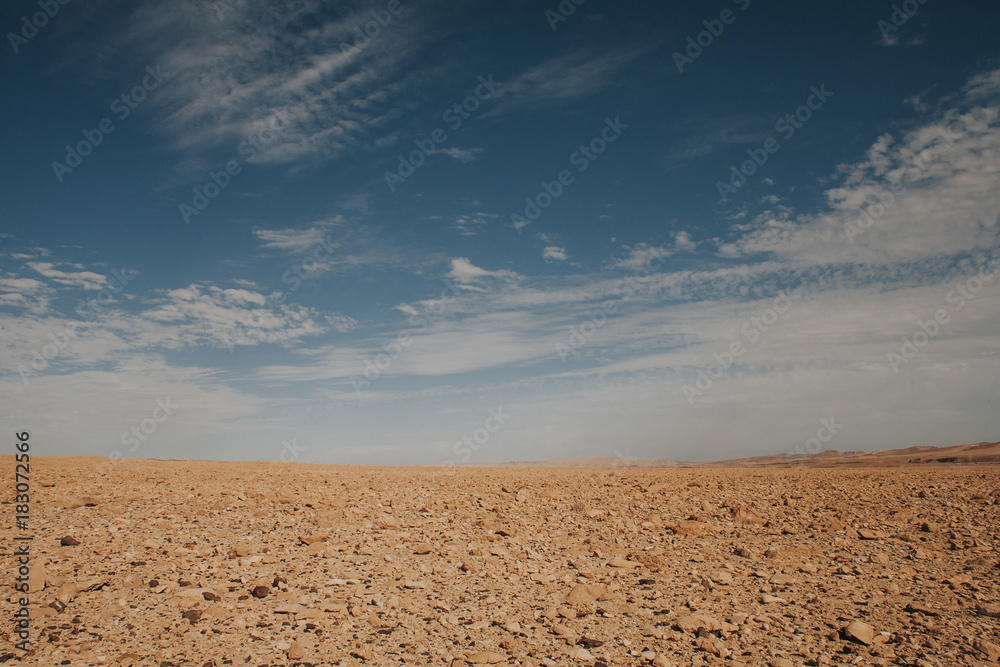Empty desert area horizon line. Dry ground with blue cloudy sky over the sand.