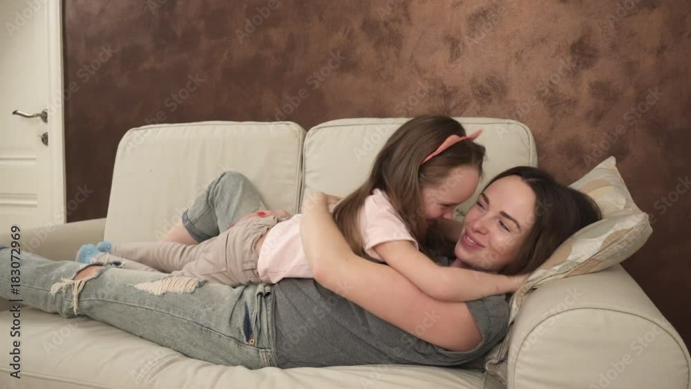 Happy mother and little daughter embrace and tickle lying on the couch Happy mother and little daughter embrace and tickle lying on the couch