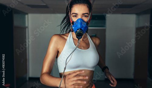 Sportswoman with mask running on treadmill in gym photo