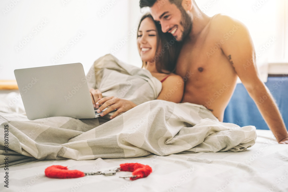 Happy young couple lying on a bed with computer