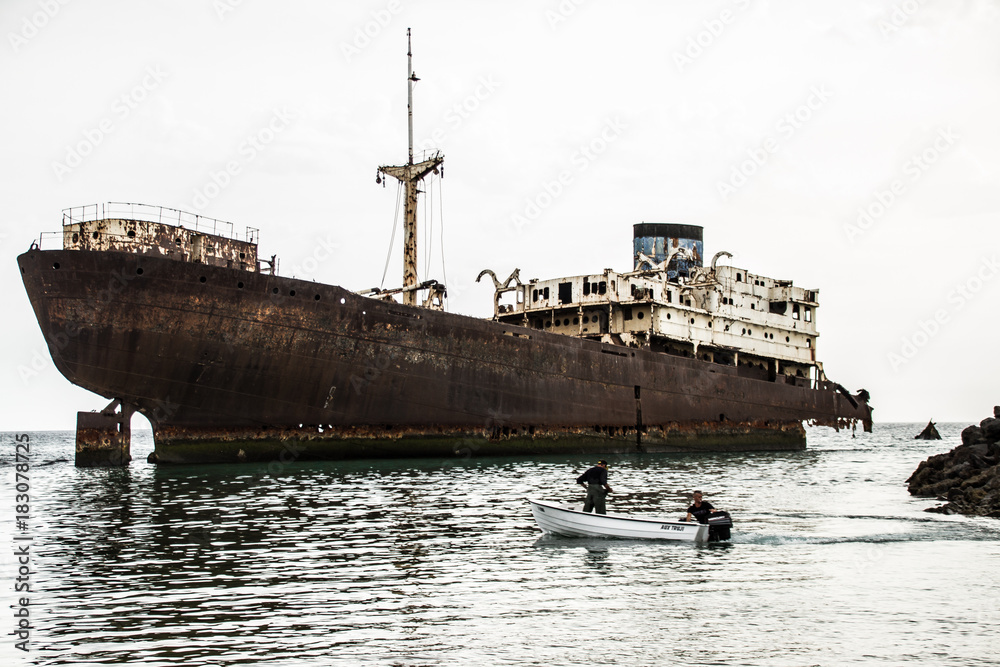 An old shipwreck above sea level. a metal ship with a small boat heading towards it. An old shipwreck above sea level. a metal ship with a small boat heading towards it.