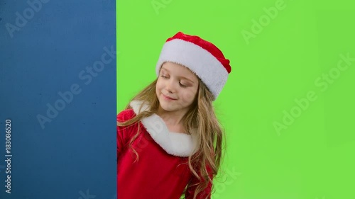 Child girl peeking out from behind the blue board. Green screen. Slow motion photo