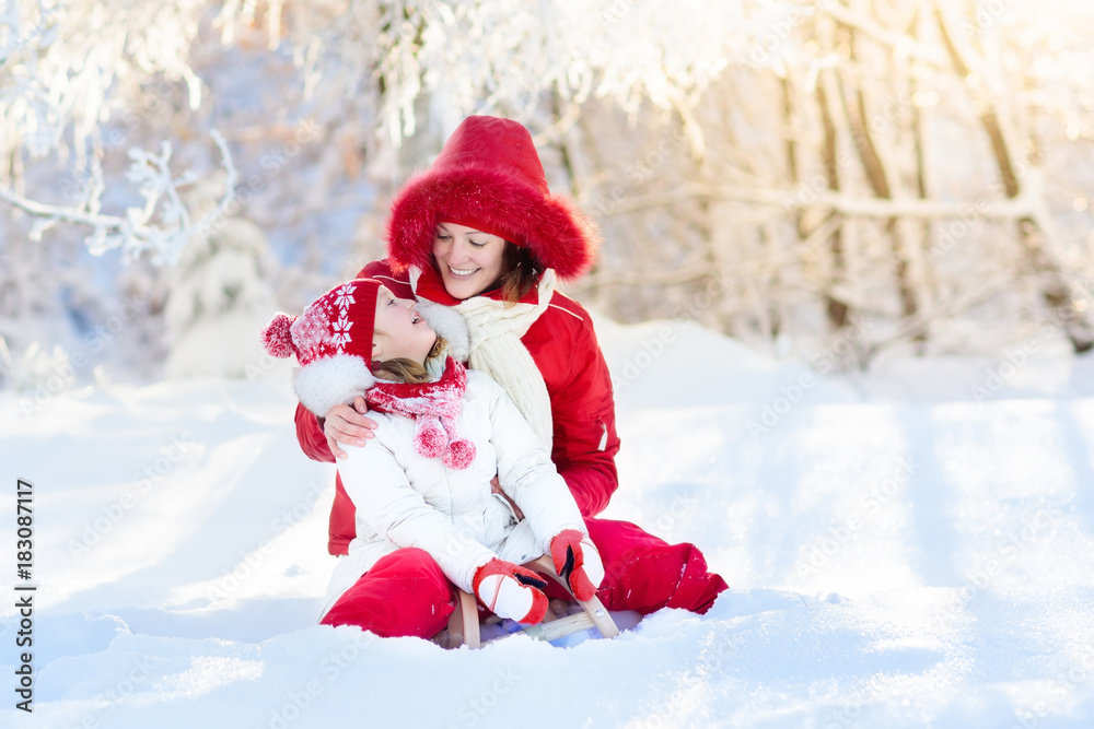 Mother and child sledding. Winter snow fun. Family on sleigh.