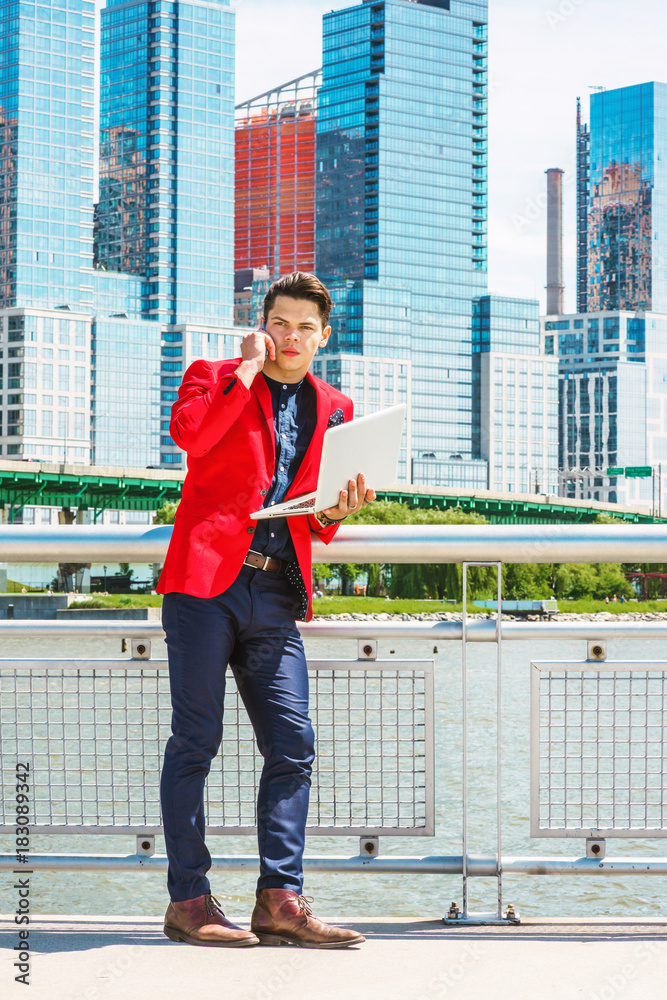 Businessman traveling, working in New York. Dressing in red blazer, blue collarless shirt, a guy standing in busy business district, talking on mobile phone, working on laptop computer in same time..