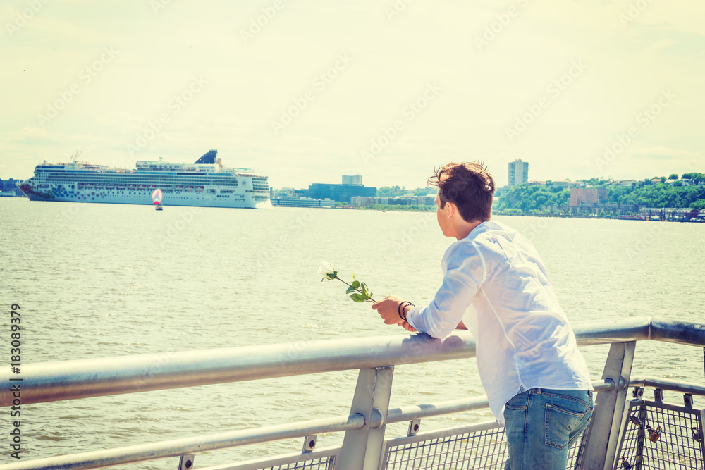 Man Welcomes You. Wearing white shirt, holding white rose, a guy standing by Hudson River in New York, opposite New Jersey, looking faraway. Boat, ship on background. Copy Space..