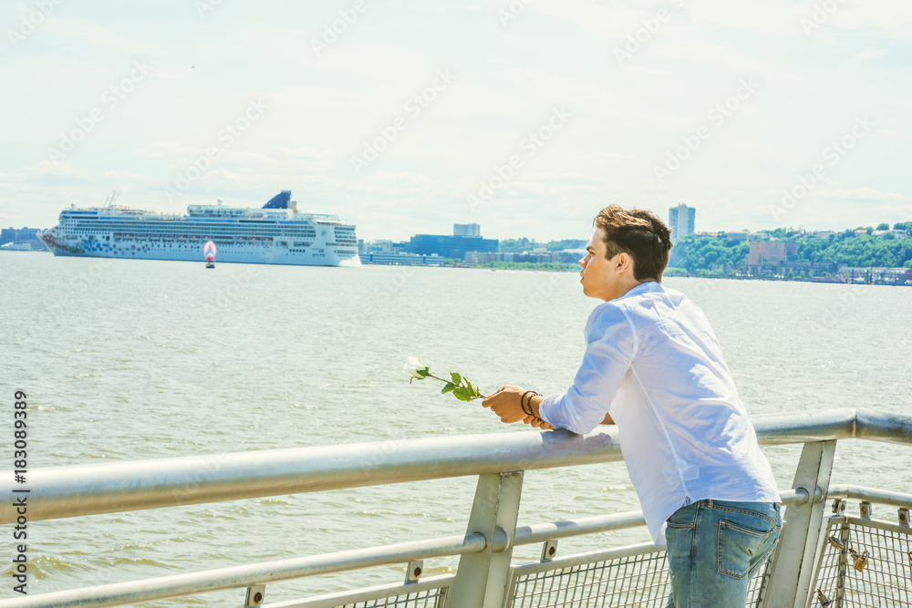 Man Missing You. Wearing white shirt, jeans, holding white rose, a guy standing by Hudson River in New York, opposite New Jersey, thinking, lost in thought. Concept of looking for love, friendship..