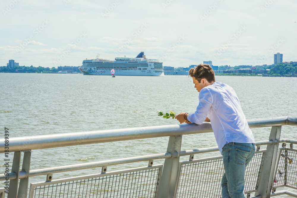 Lonely man thinking you. Wearing white shirt, holding white rose, a guy standing by Hudson River in New York, opposite New Jersey, looking down, sad, thinking. Boat, ship on background. Copy Space..