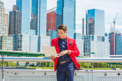 Businessman traveling, working in New York. Dressing in red blazer, blue collarless shirt, a guy standing in busy business district, looking down, reading, working on laptop computer. Copy Space.. photo