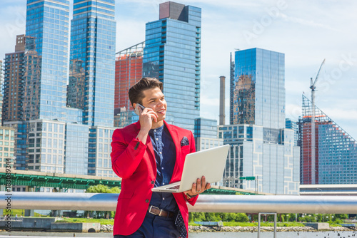 Businessman traveling, working in New York. Dressing in red blazer, blue collarless shirt, a guy standing in busy business district, talking on mobile phone, working on laptop computer in same time..