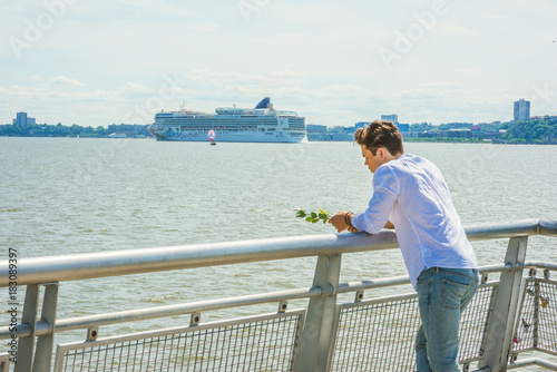 Lonely man thinking you. Wearing white shirt, holding white rose, a guy standing by Hudson River in New York, opposite New Jersey, looking down, sad, thinking. Boat, ship on background. Copy Space.. © Alexander Image