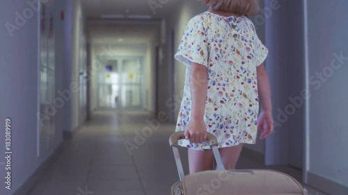 A little girl is rolling a suitcase in a hotel. Low angle shot.
