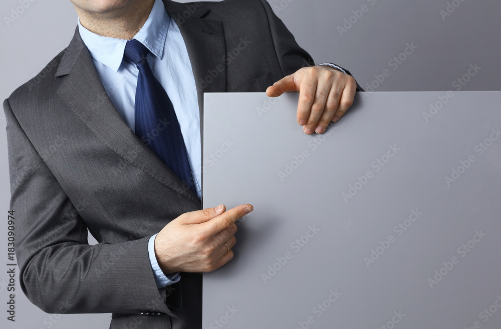 Businessman holding a blank board standing on gray background Businessman holding a blank board standing on gray background