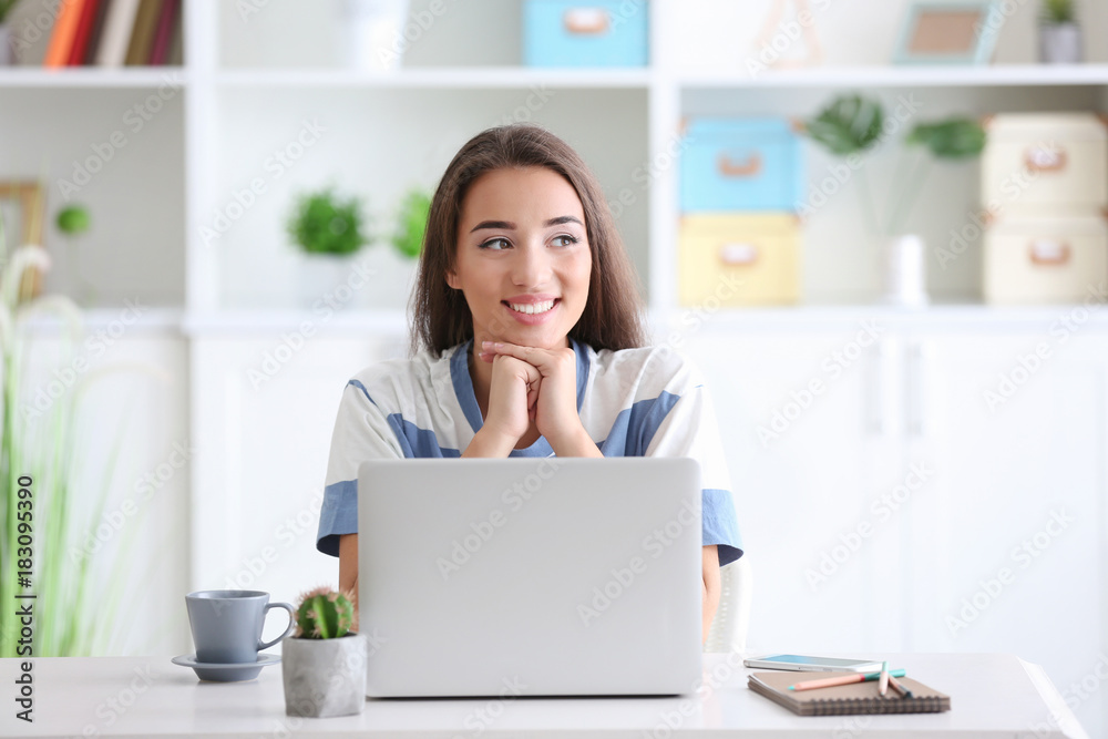 Young woman using laptop while sitting at table indoors Young woman using laptop while sitting at table indoors