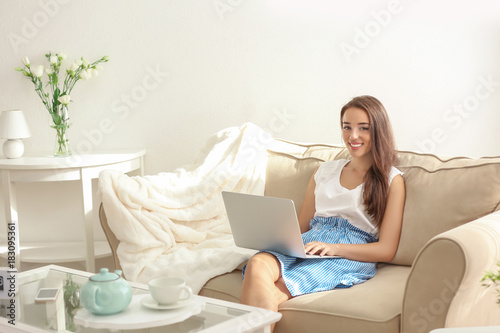 Young woman using laptop while sitting on cozy sofa indoors