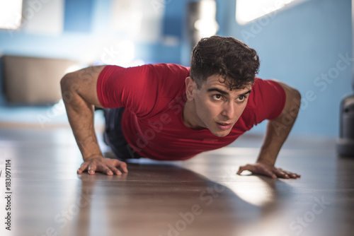 Young man trains push-ups in the gym on hands indoors