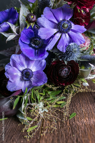 nature, flower arranging, hobby concept. close up of great lilac anemons with puffy black centers that placed in the bouquet decorated with various leaves and battercups photo