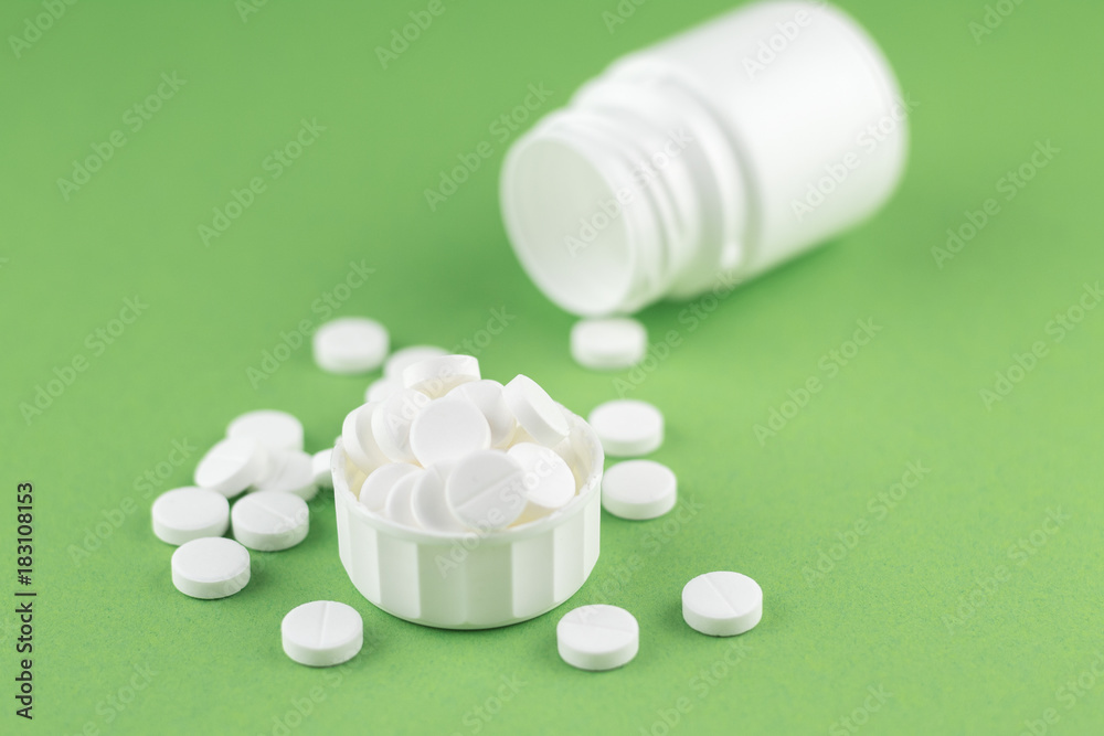 Close up white pill bottle with spilled out pills and capsules in cap on pistachio green background with copy space. Focus on foreground, soft bokeh. Pharmacy drugstore concept Close up white pill bottle with spilled out pills and capsules in cap on pistachio green background with copy space. Focus on foreground, soft bokeh. Pharmacy drugstore concept
