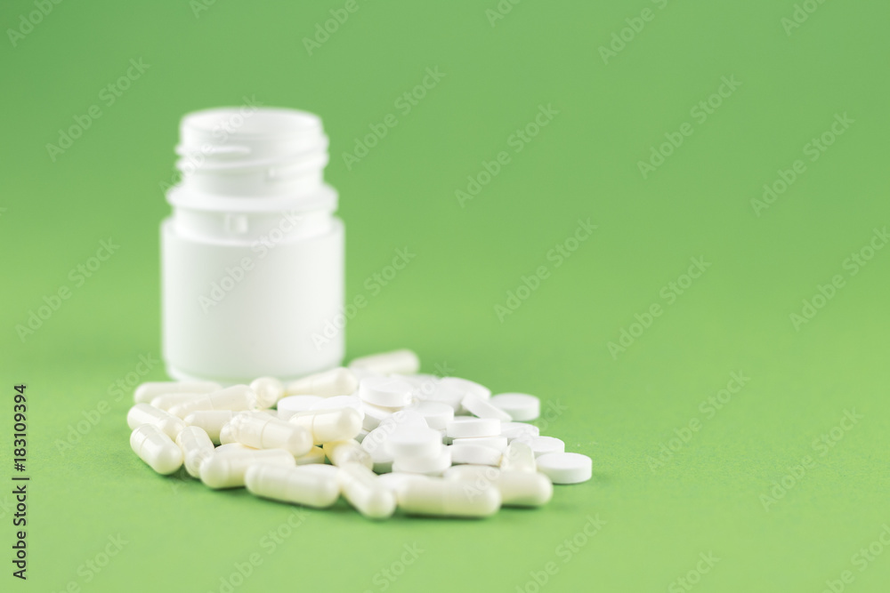 Close up white pill bottle with spilled out pills and capsules on pistachio green background with copy space. Focus on foreground, soft bokeh. Pharmacy drugstore concept Close up white pill bottle with spilled out pills and capsules on pistachio green background with copy space. Focus on foreground, soft bokeh. Pharmacy drugstore concept