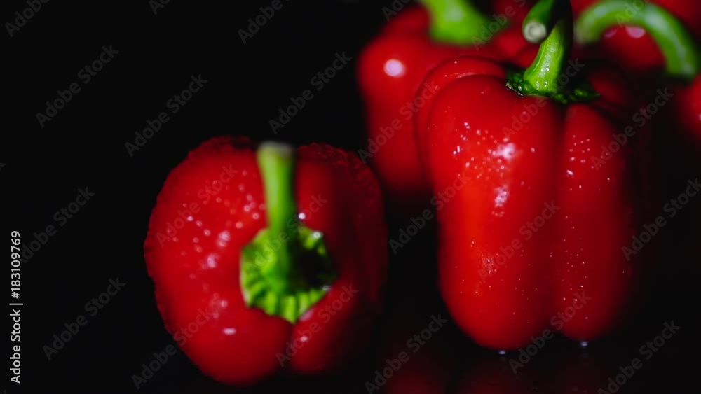 Fresh red peppers freshly washed drops flow down on the table. Closeup rotating on black background.