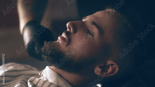 The barber shaves his head, mustache and beard to the man in the barbershop. The stylist uses a classic sharp razor, neatly shaving the client.