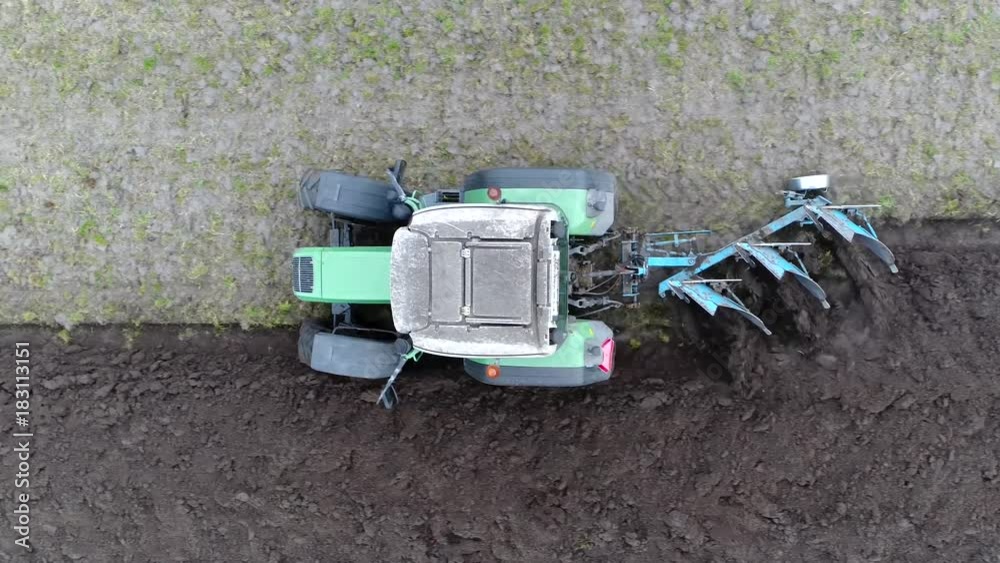 Aerial top-down view of modern tractor ploughing or plowing rough land for initial cultivation of soil in preparation for sowing seed or planting to loosen or turn soil stable footage above tractor 4k