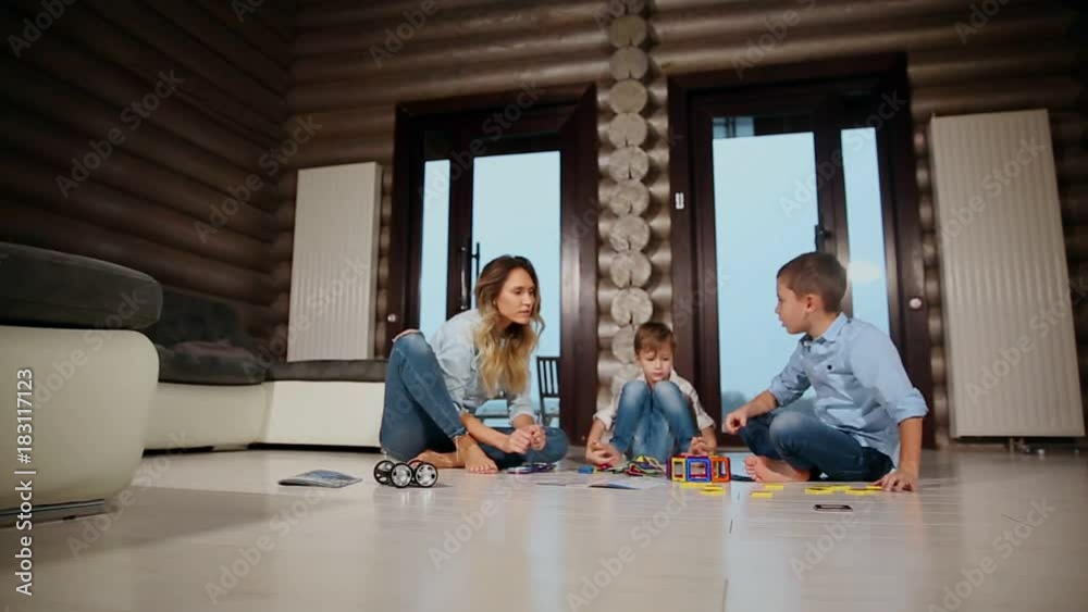 Happy mother with two children sitting on the floor of his country house spending time together collecting children's designer. Living room with panoramic Windows. Happy mother with two children sitting on the floor of his country house spending time together collecting children's designer. Living room with panoramic Windows.