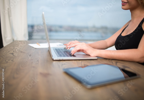 Hipster girl professional content writer keyboarding on laptop computer, sitting at the wooden table with touch pad. Woman skilled freelancer or copywriter typing text on website via net-book