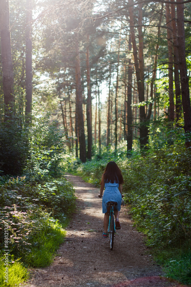 Photo of a young pretty girl riding a bicycle in a forest on a sunny summer day