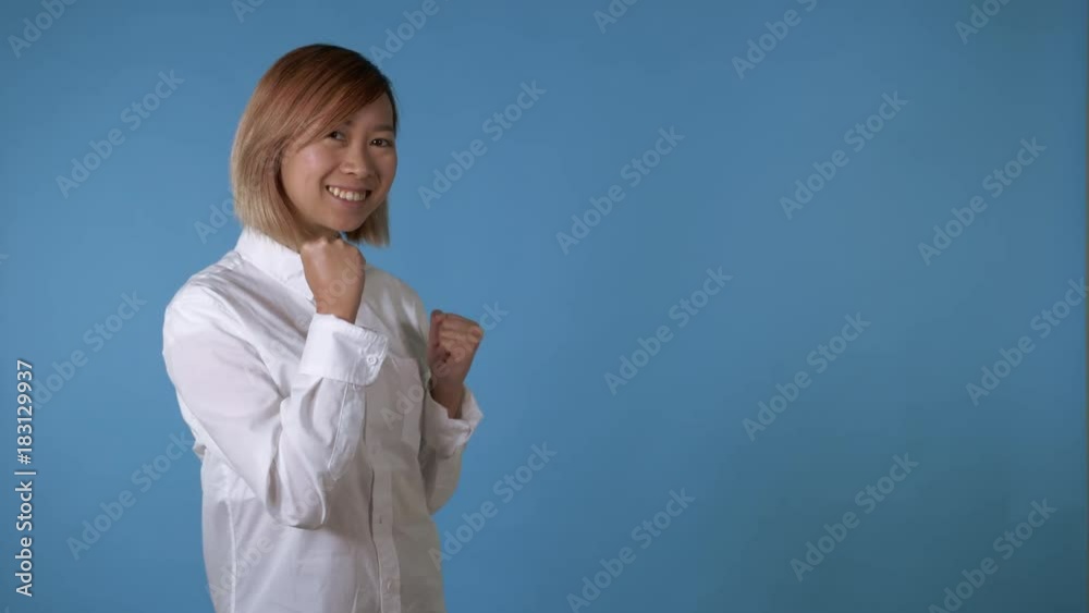 portrait young asian female posing happy dancing on blue background in studio. attractive korean woman with blond hair wearing white casual shirt looking at the camera. portrait young asian female posing happy dancing on blue background in studio. attractive korean woman with blond hair wearing white casual shirt looking at the camera.