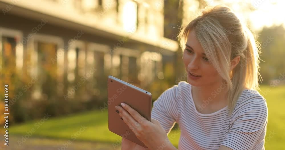 Young female student using tablet computer in the park. Girl doing online shopping on tablet pc