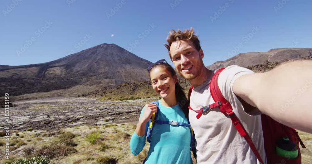 Happy Backpacking Couple Taking Selfie Video on Travel on New Zealand Hiking Tongariro Alpine Crossing. Couple photographing themselves by volcano. Beautiful landscape in Tongariro National Park. Happy Backpacking Couple Taking Selfie Video on Travel on New Zealand Hiking Tongariro Alpine Crossing. Couple photographing themselves by volcano. Beautiful landscape in Tongariro National Park.
