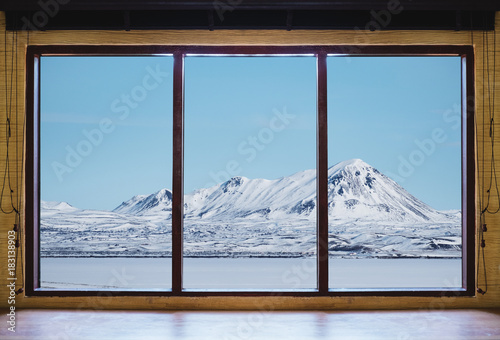 Fototapeta Patrząc przez okno w zimie, drewniane ramy okna z biurka i krajobraz śnieg góry i zamarznięte jezioro widok w Islandii