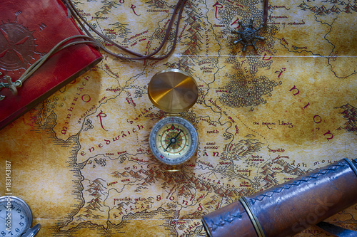 An ancient map (possibly pirate or treasure or middle-earth) with a compass in the center and other adventure attributes stuff (notepad, telescope and pocket watch) around the perimeter photo